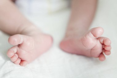 Bebeğin küçük bacakları, beyaz çarşafların üzerine uzanmış, yakın görüş.