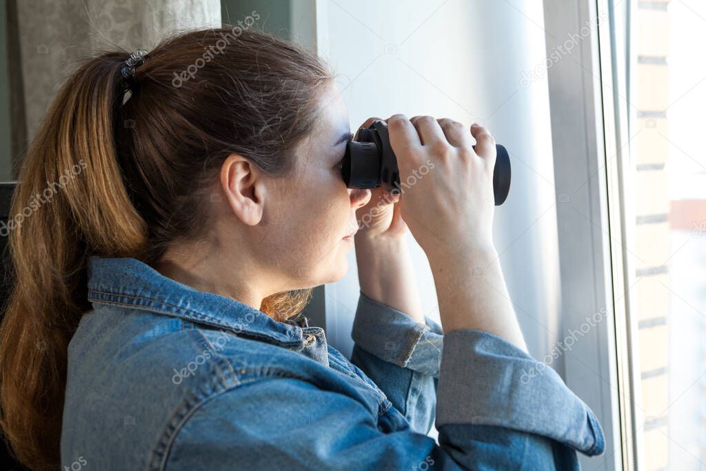 Nosy woman peering through window with binoculars, domestic room