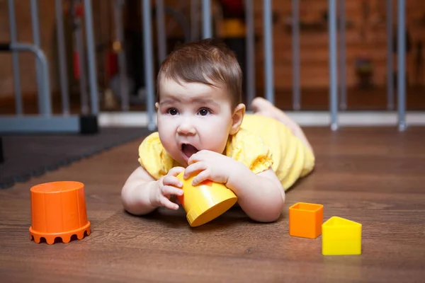 小女孩7个月大 躺在硬木地板上咀嚼着刚出世的玩具 — 图库照片