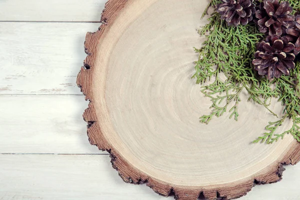 Деревянная доска с листьями туи и сосновыми шишками на деревянном столе — стоковое фото