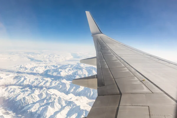 Vista do assento da janela do avião enquanto voa sobre montanhas nevadas — Fotografia de Stock