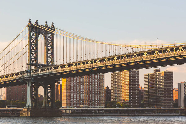 Manhattan bridge in New York at sunset with residential buildings on background. Golden reflections on the bridge and on the houses. Travel and architecture concepts