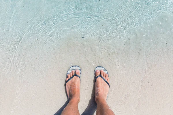 Male feet wearing female flip flops at beach — Stock Photo, Image