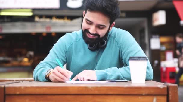 Hombre con auriculares leyendo y escribiendo un documento — Vídeo de stock