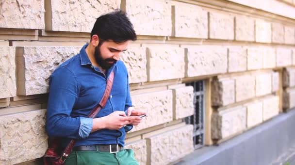 Hombre escribiendo en el teléfono inteligente y apoyado en una pared — Vídeo de stock