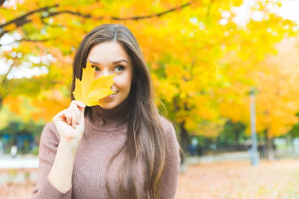 Leende kvinna porträtt med ett gult löv på hösten — Stockfoto