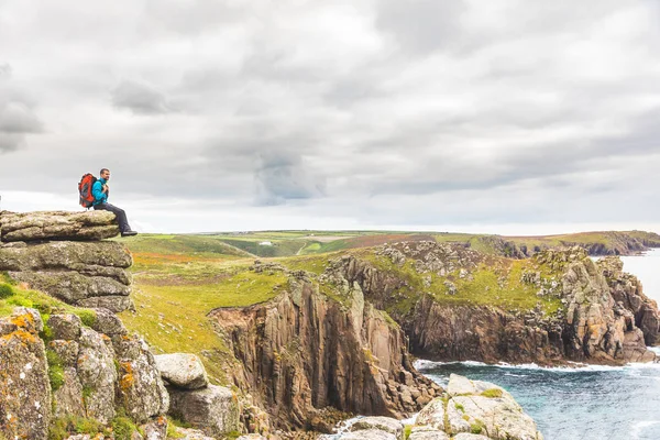 Uomo seduto su una scogliera rocciosa godendo la vista — Foto Stock