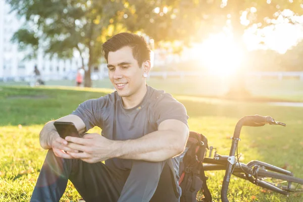 Man met de fiets via telefoon op park bij zonsondergang — Stockfoto