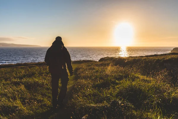Man with backpack walking toward the sea at sunset — Stock Photo, Image