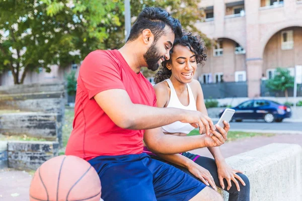 Black couple with phone and basketball at park