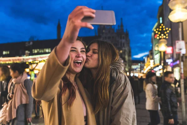 Chicas felices tomando una selfie juntos en el mercado de Navidad Munich —  Fotos de Stock