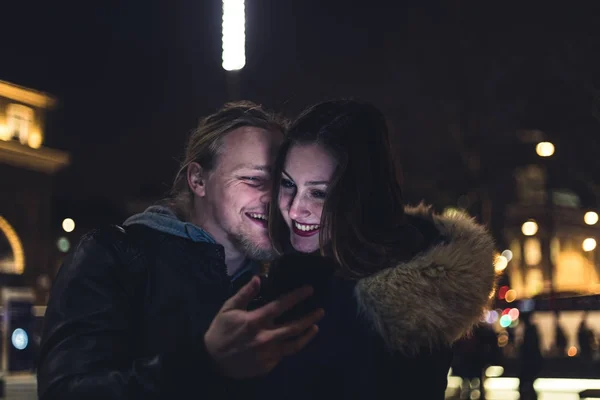 Счастливая пара на улице зимой смотрит на телефон — стоковое фото