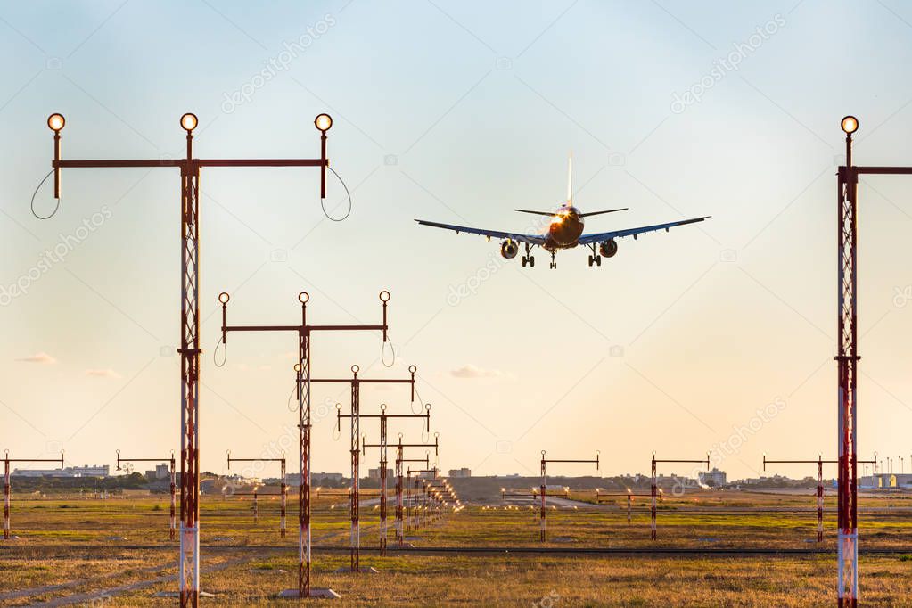 Airplane landing at sunset, rear view with approach lighting sys