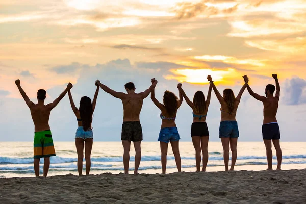 Skupina přátel, zvyšování rukou na pláži při západu slunce — Stock fotografie