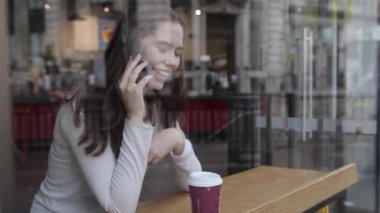 Bir kafede kahve içen ve akıllı telefon kullanan genç bir kadın.