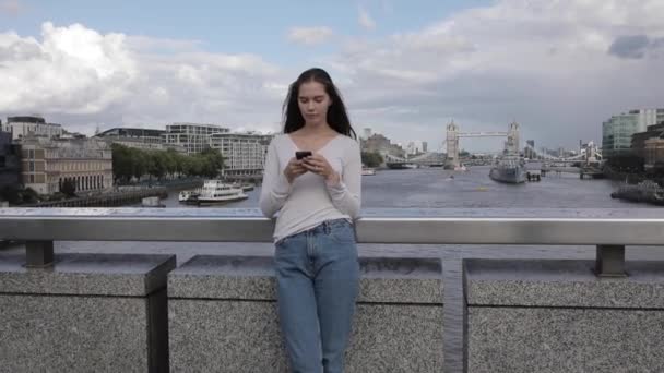 Vrouw typt aan de telefoon in Londen met Tower Bridge op de achtergrond en mensen — Stockvideo