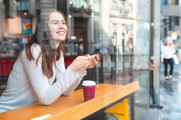 Glückliche Frau im Café, die mit ihrem Smartphone SMS schreibt — Stockfoto