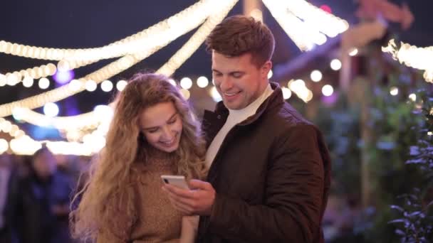 Ευτυχισμένο ζευγάρι διασκεδάζει στο λούνα παρκ και κοιτάζοντας το κινητό τηλέφωνο — Αρχείο Βίντεο