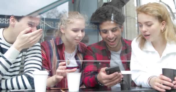 Glade multiraciale venner ser på en smartphone i en cafe og griner – Stock-video