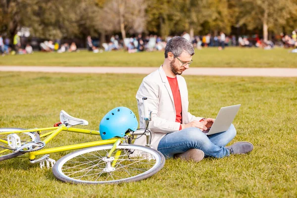 Professional man working with laptop computer at park in London - Young business man sitting on the grass, with fixed gear bike next to him - Smart casual clothing, lifestyle and technology concepts