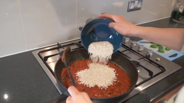 Cooking risotto rice with tomato sauce - close up of female hands and skillet — Stock Video