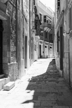 Malta adasında tipik bir dar sokak. Valletta 'nın tarihi bölümünde geleneksel renkli Malta balkonları olan binalar. Siyah beyaz resim