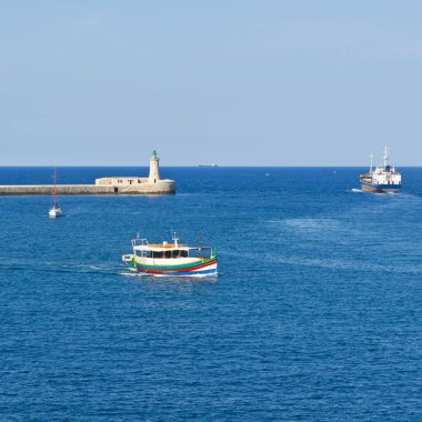 Kargo gemisi Valletta limanından ayrılıyor. Deniz fenerleri Malta limanlarının girişini gösteriyor. Körfez havzasında eğlence gemisi