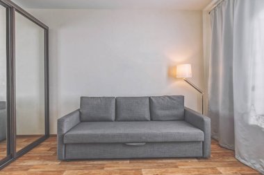 Gün ışığında küçük, samimi bir stüdyo daire. Mavi, basit bir kanepe ve pencere.