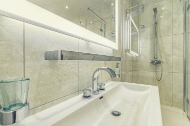 Duş kabini ve lavabosu olan parlak, temiz, küçük bej bir banyo.