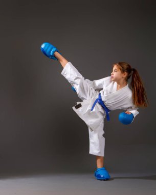 Mavi kemerli, beyaz kimonolu küçük bir kız karanlık arka planda darbeler indiriyor.