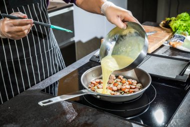 Tavada soğanlı ve sosisli omlet pişir.