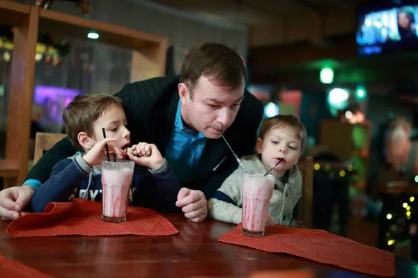 Отец и двое сыновей пьют молочный коктейль — стоковое фото