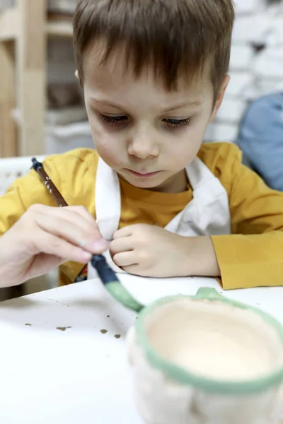 Child paints clay pot — Stock Photo, Image