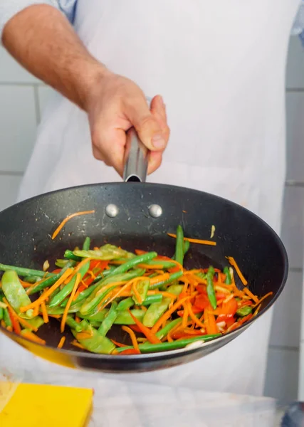 Рука тримає смажені овочі на сковороді — стокове фото