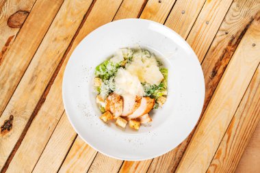 Beyaz tabakta taze sezar salatası, ahşap arka plan.