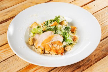 Beyaz tabakta taze sezar salatası, ahşap arka plan.