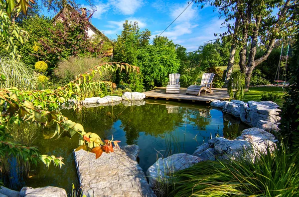 Deckchairs near pond in green blooming garden — Stock Photo, Image