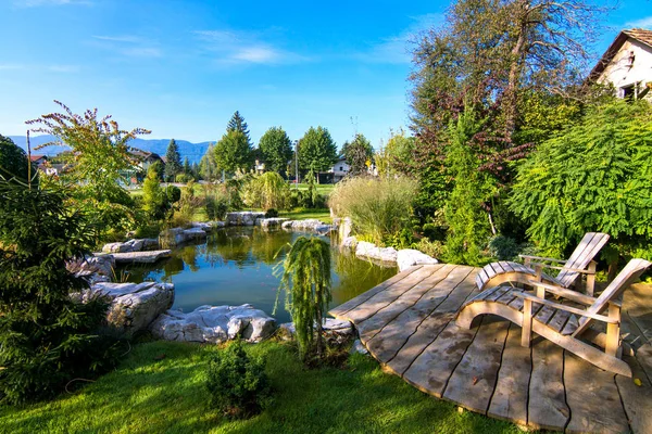 Solstolar nära pond i gröna blommande trädgård — Stockfoto