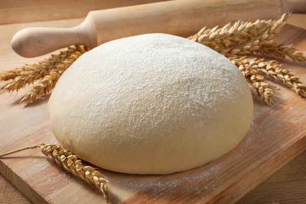 Fresh dough on a board with ears of wheat and rolling pin. — Stock Photo, Image