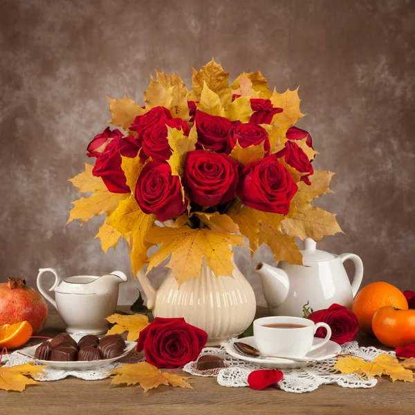 Mesa com xícaras de chá, chocolates e um buquê de rosas — Fotografia de Stock