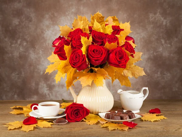 Cups of tea, chocolates and a bouquet of roses and aunumn leaf. — Stock Photo, Image