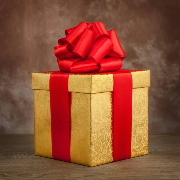 Golden gift box with a red bow on an old table — Stock Photo, Image