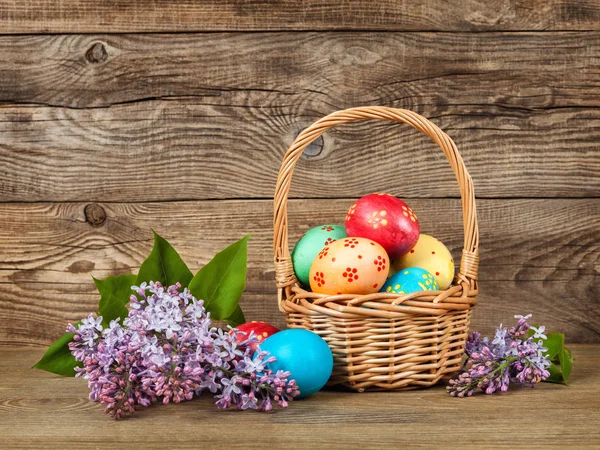 Lilac and gold easter eggs in a basket on an old board — Stock Photo, Image