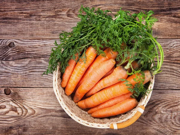 Rijpe wortelen in een mandje op een oude tafel — Stockfoto