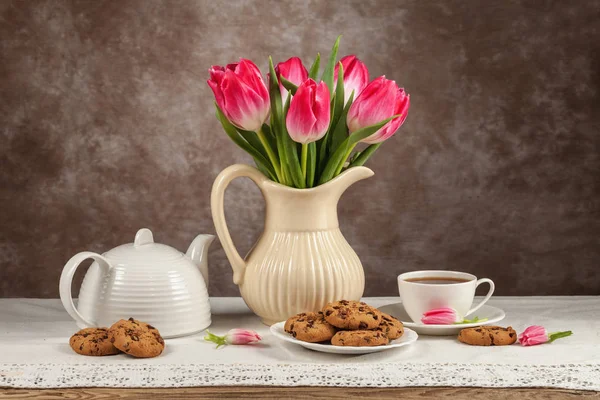 Tulipanes en un jarrón, té, chocolates en el tablero — Foto de Stock