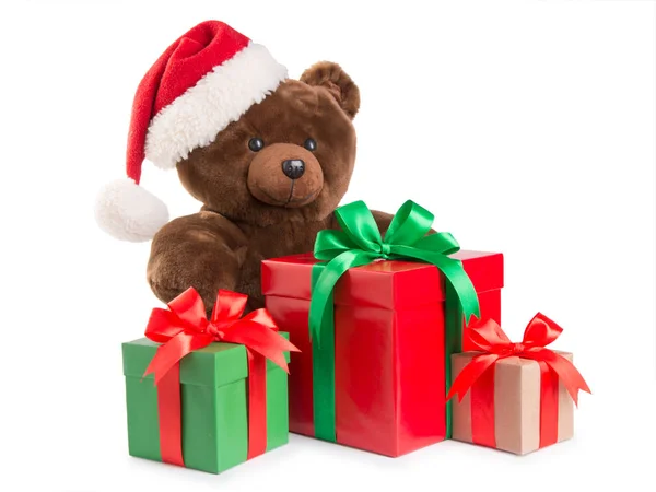 Osito de peluche en un sombrero de santa y regalos aislados en blanco — Foto de Stock