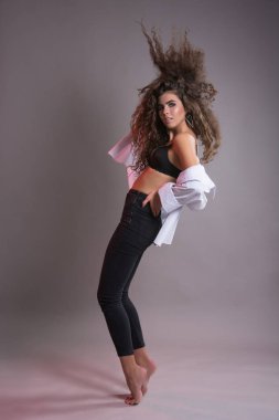 Studio gri bir arka plan üzerinde siyah kıvırcık saçlı oldukça ince kız