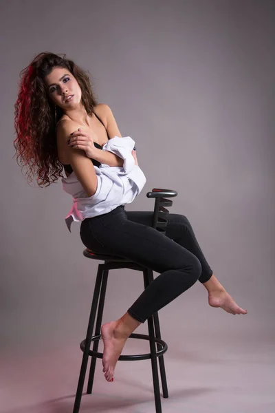 Studio gri bir arka plan üzerinde siyah kıvırcık saçlı oldukça ince kız