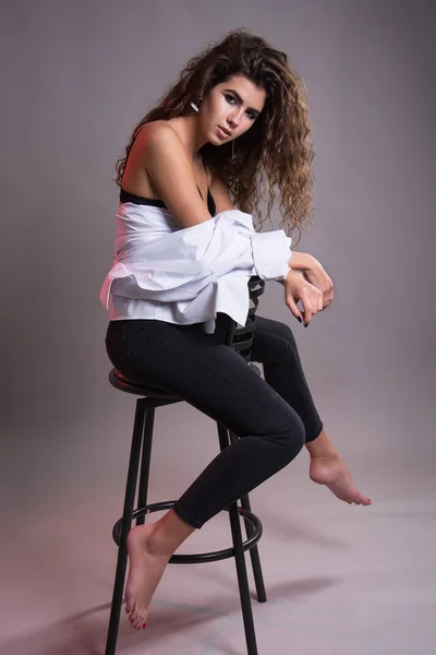 Studio gri bir arka plan üzerinde siyah kıvırcık saçlı oldukça ince kız