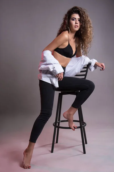 Studio gri bir arka plan üzerinde siyah kıvırcık saçlı oldukça ince kız